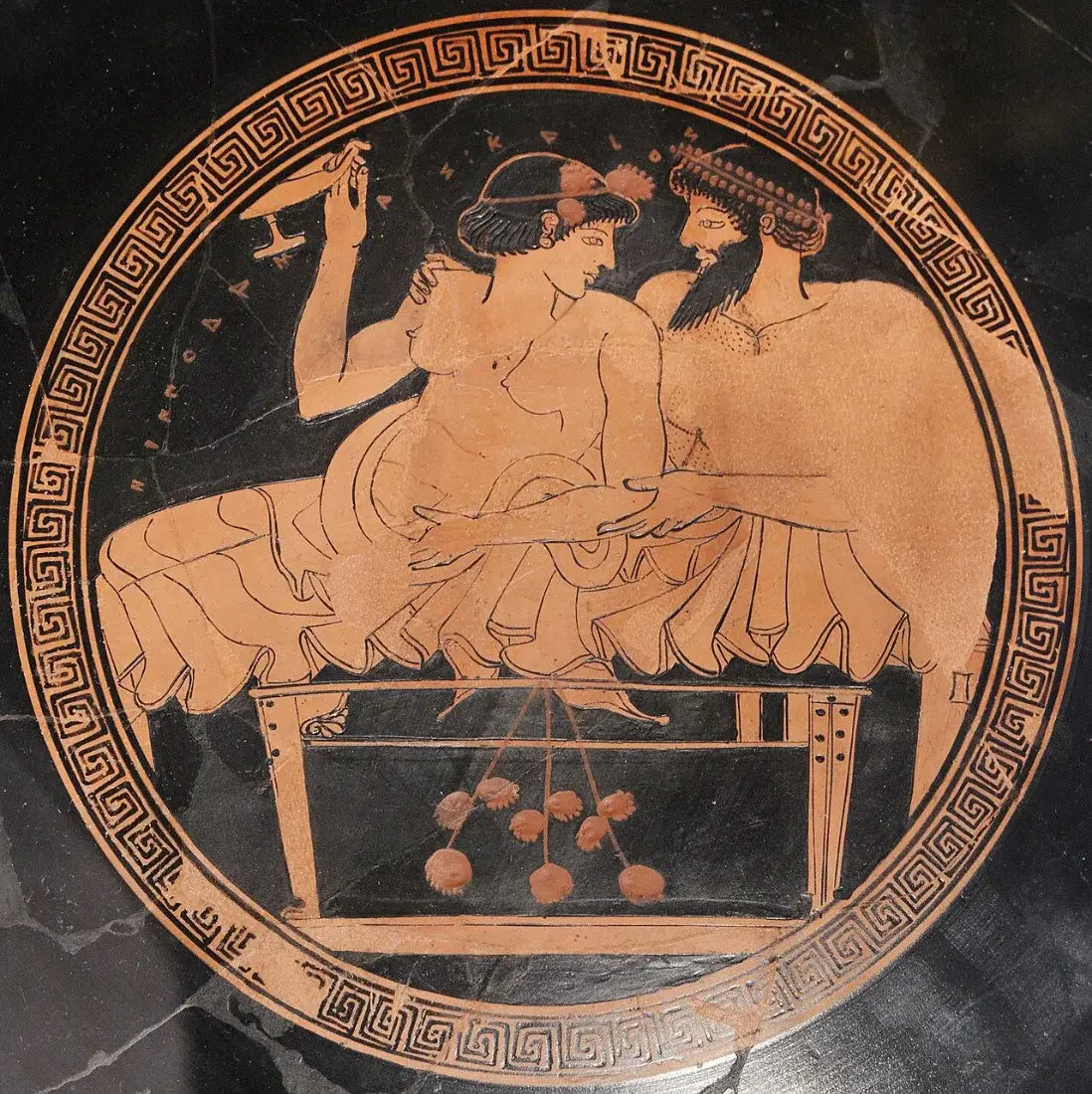 A round painting inside a cup: two figures recline on a couch, a cup in hand.