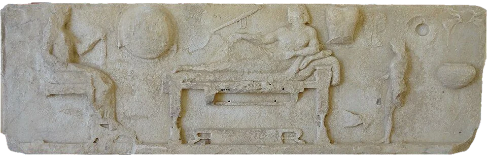 Marble relief: a man reclining on a couch and a woman seated beside him.