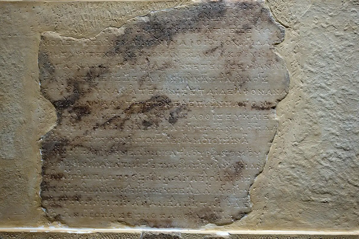 A worn marble block covered with small lines of Greek letters, with smaller letters set above the lines of text.