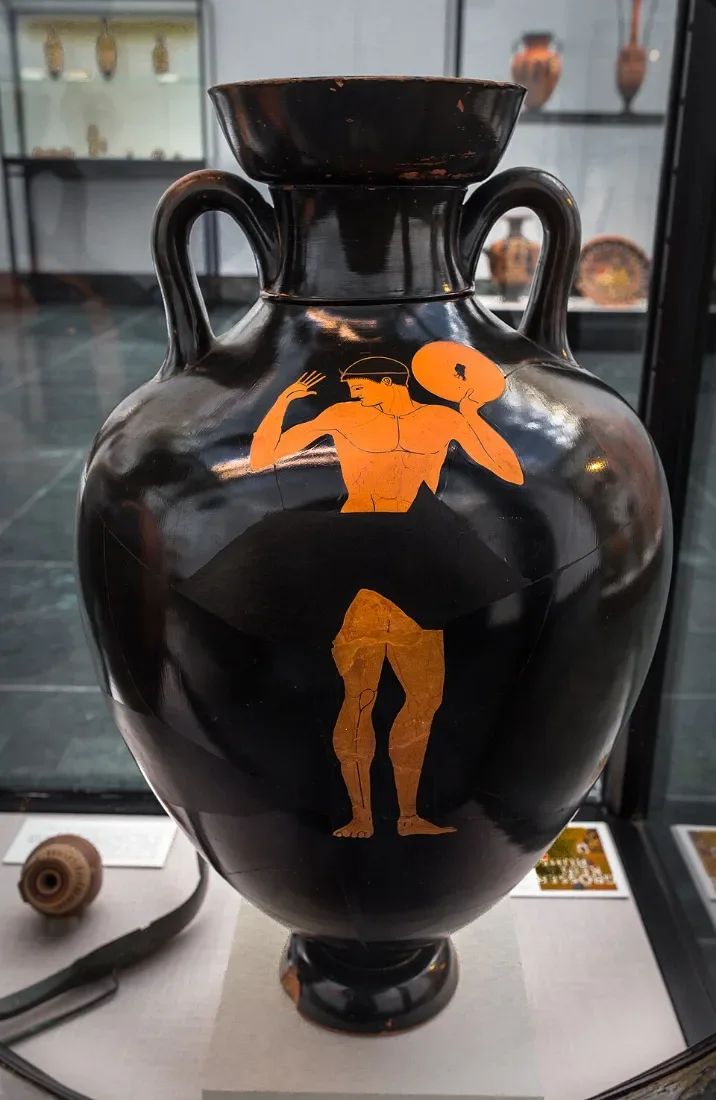 A black amphora with a single red figure of an athlete holding a discus.