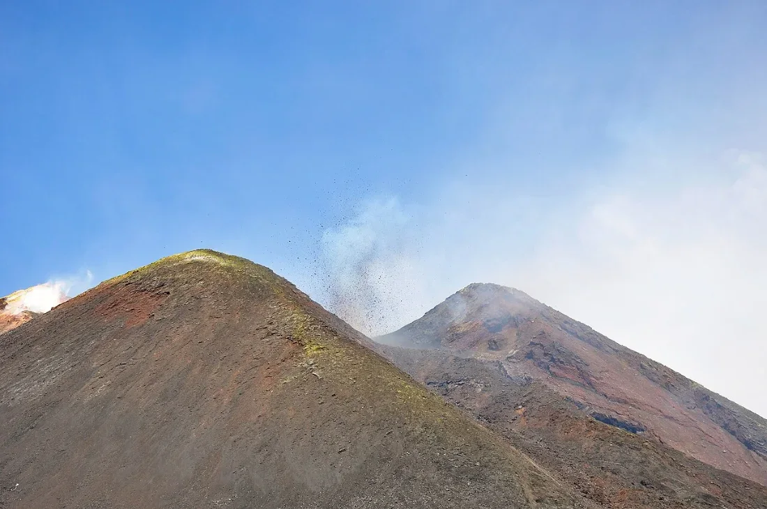 Two volcanic cones with a plume of smoke under a blue sky.