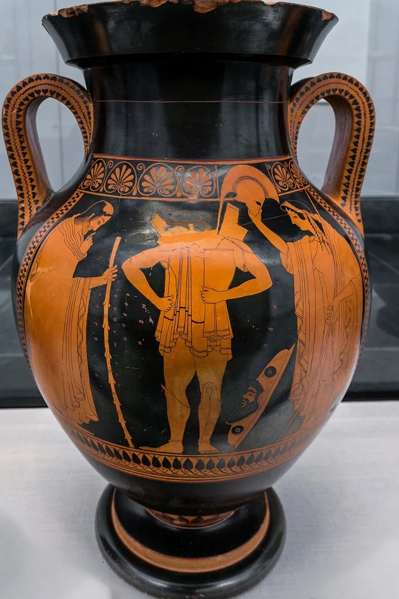 A red-figure amphora: a young warrior fastening his armour between an old man with a staff and a woman.