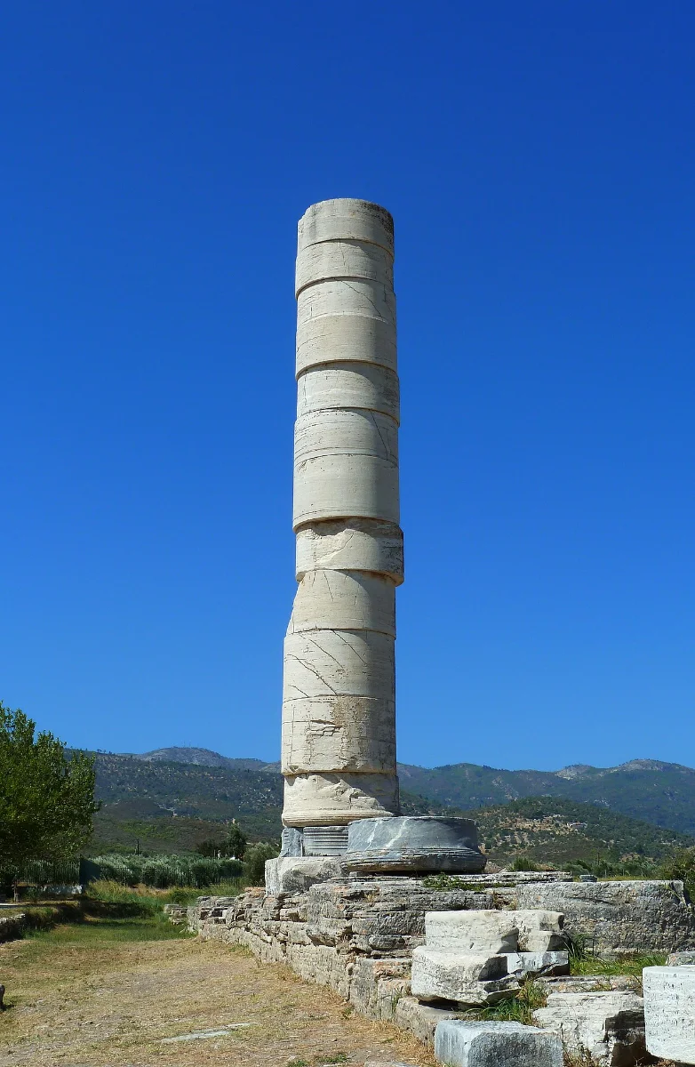 A single tall column, reassembled from drums, standing among ruins under a blue sky.