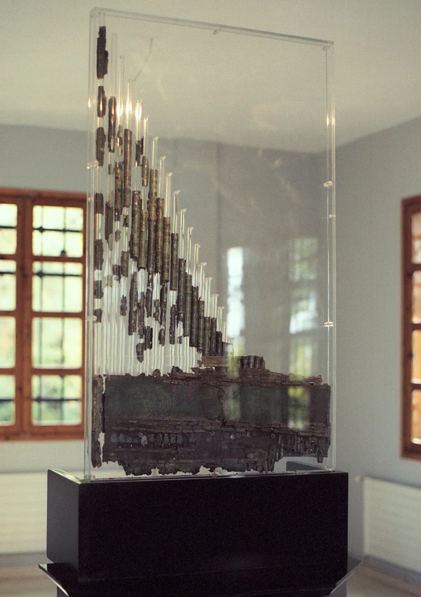 Remains of an ancient organ shown in a glass case: a row of bronze pipes of graded length above a base.