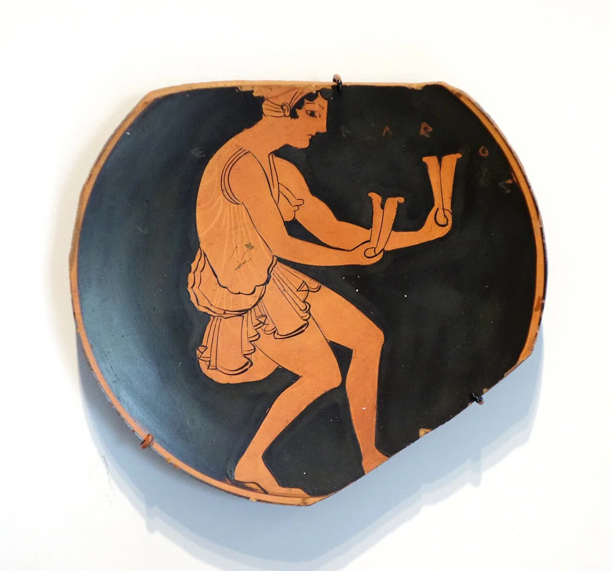 Red-figure cup interior: a woman dances with a pair of clappers in each hand.