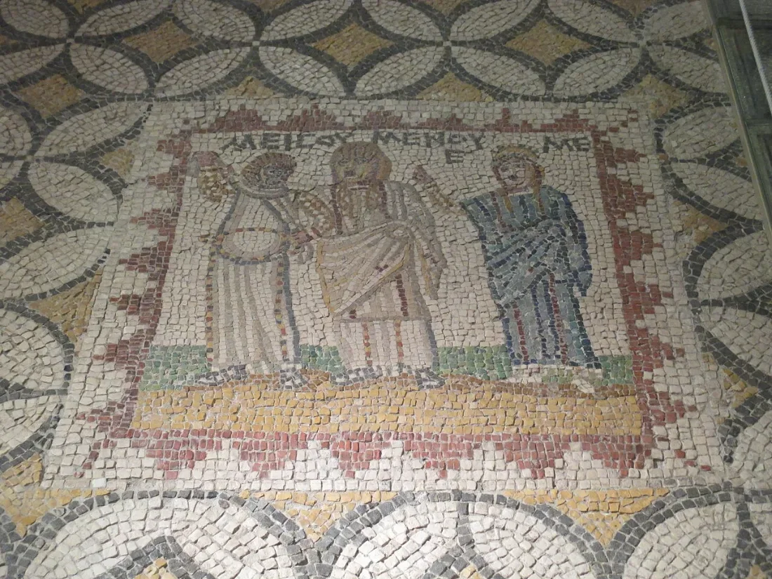 A floor mosaic with three figures in a panel with a Greek inscription.