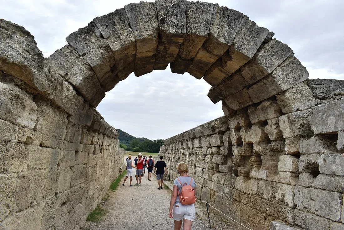 A stone tunnel with a round arch opening on to a sunlit track.