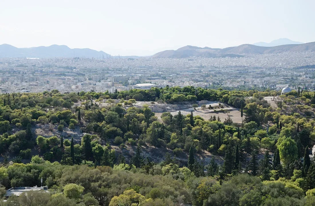 A wooded hill seen from above, with the city of Athens behind.