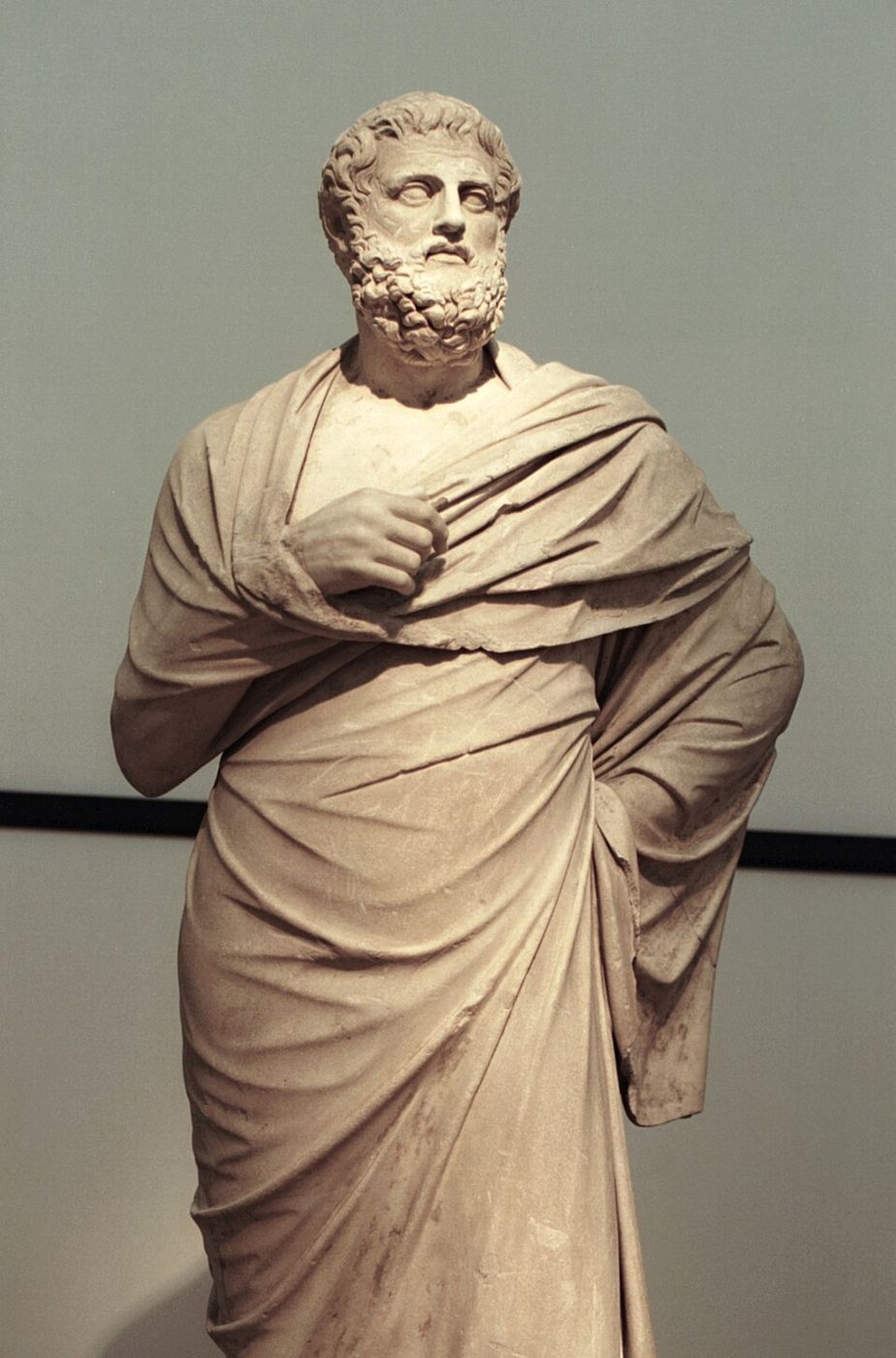 Marble statue of a bearded man standing wrapped in a cloak.