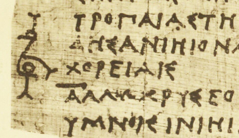 Detail of papyrus with Greek capitals and an ornate sign in the margin.