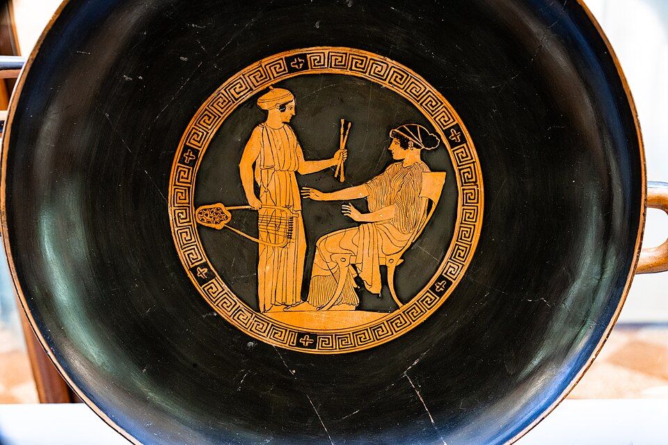 Red-figure cup interior: a standing woman holding a lyre and auloi before a seated woman.